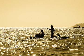 Silhouette of a young couple paddling on a surf at sunset in Maro, Andalusia, Spain. © Giulio