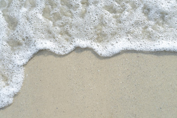 Fototapeta na wymiar Soft wave of the sea on the sandy beach with white clean foam water surf. Top view with copy space.