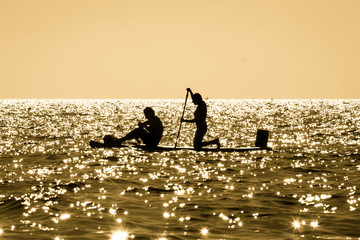 Silhouette of a young couple paddling on a surf at sunset in Maro, Andalusia, Spain. © Giulio