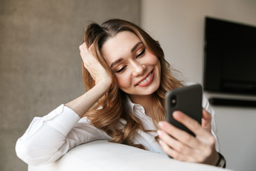 Beautiful young business woman dressed in formal clothes shirt indoors using mobile phone.