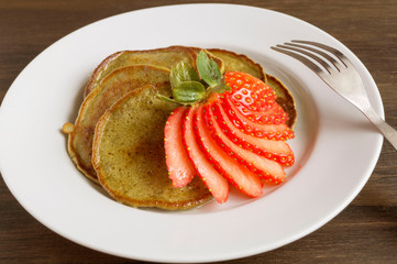 Vegetarian pancakes with ripe strawberries. on a wooden table.