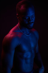 Fototapeta na wymiar Red and blue lighted portrait of young and sexy muscular shirtless man with neck chain.