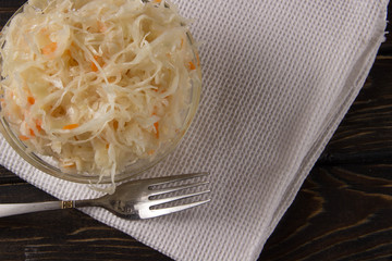 Sauerkraut with carrots in a glass bowl on a dark wooden background with a white towel