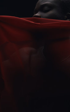 Art portrait of black man posing behind red fabric. Sensual. Art performance, acting. Dark key