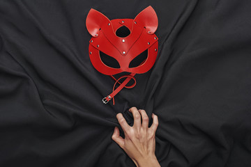 Sexual Pleasure. Top view of hand touching black silk fabric and red bdsm leather mask - obrazy, fototapety, plakaty