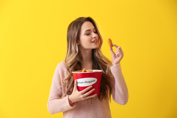 Beautiful woman with bucket of tasty nuggets on color background