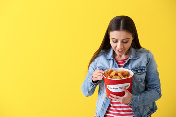 Beautiful woman with bucket of tasty nuggets on color background