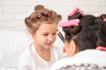 Young mother applying cosmetics onto face of her cute daughter at home