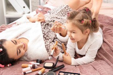 Cute daughter and mother with makeup cosmetics lying on bed