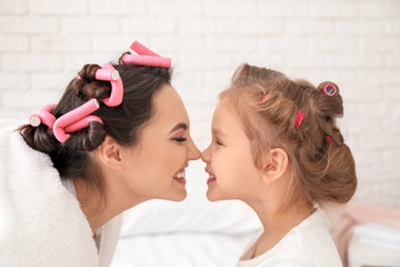 Portrait of young mother with cute little daughter with hair curlers at home