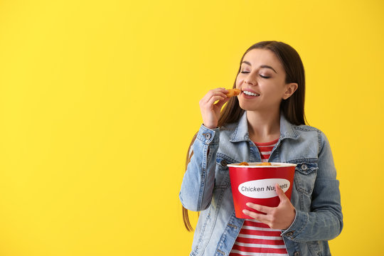 Beautiful woman with bucket of tasty nuggets on color background