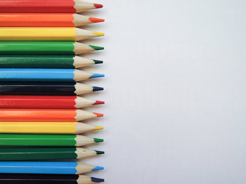 Multicolored bright pencils of the same size lie flat on white paper, separated by the colors of the rainbow.