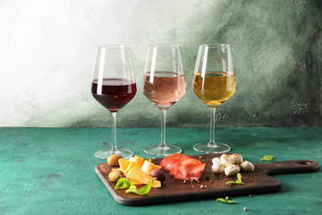 Glasses of different sorts of wine with snacks on color table