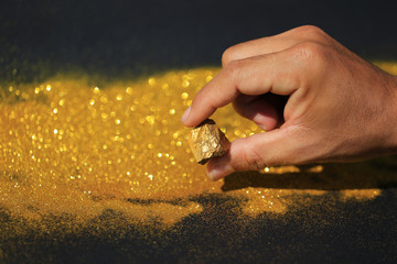 Man hand holding pure gold minerals with golden light on black background, investment and business...