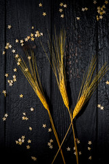 Horizontal composition still Life with wheat ears on a background of black burnt boards with scattered pastry stars. The concept of family happiness