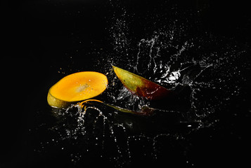 Ripe cut mango with water splash on dark background