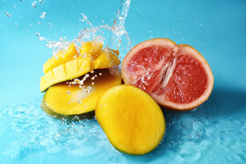 Fototapeta na wymiar Ripe cut fruits with water splash on color background