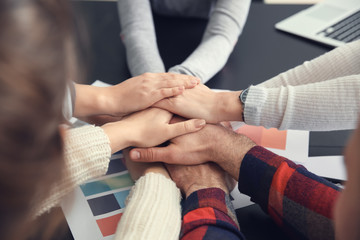 Group of people putting hands together as symbol of unity in office