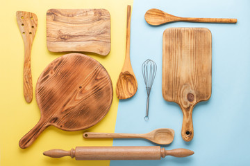 Kitchen utensils, food preparation cooking accessorises, chopping boards, wooden spoons, whisk on blue and yellow table, top view, selective focus