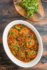 Chopped fish cutlets in spicy tomato sauce with fresh mint. White dish on wooden rustic table, top view