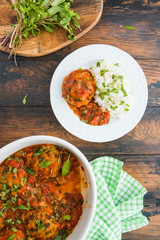 Fish rissoles  in spicy tomato sauce with fresh mint and boiled rice. White dish and plate on wooden rustic table, top view