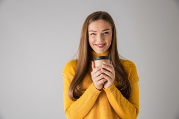 Beautiful happy young woman isolated over grey wall background drinking coffee.