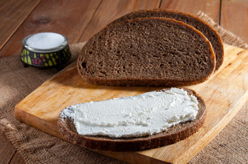Dark rye bread and sandwich on wooden cutting board and salt in saltshaker on burlap.
