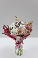A stylish bouquet of fresh rare flowers (Leukodendron, Antirium, Astrantia, Ozatamus, chrysanthemum. Main colors: white, light burgundy) in paper packaging on a light background.