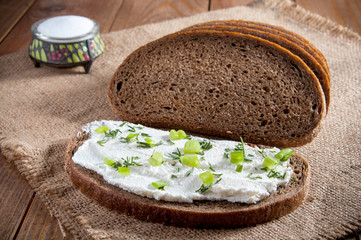 Dark rye bread, sandwich with cream, chives and dill and salt in saltshaker on burlap. Close-up.