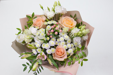 Delicate bouquet of fresh flowers (Main colors: white and pink) in a paper packaging in a vase on a light background.