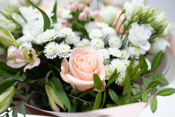 Delicate bouquet of fresh flowers (Main colors: white and pink) in a paper packaging in a vase on a light background.