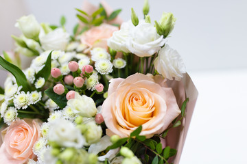 Delicate bouquet of fresh flowers (Main colors: white and pink) in a paper packaging in a vase on a light background.