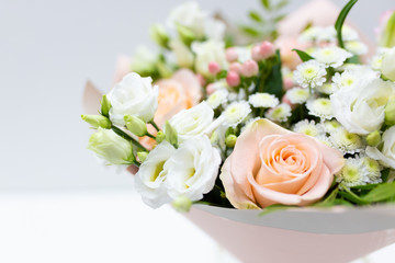 Delicate bouquet of fresh flowers (Main colors: white and pink) in a paper packaging in a vase on a light background.