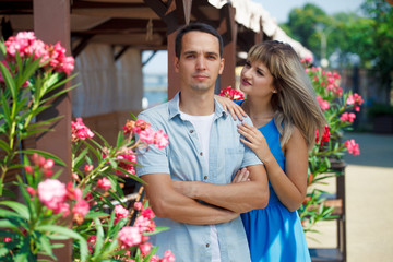Obraz premium couple, guy and girl stand on a background of flowers, hug, happy. Guy looks at the camera, the girl looks at the guy, put her hands on his shoulders. On the street. Love story