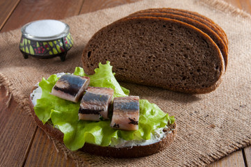 Sandwich with herring fillet, lettuce and cream. Near dark rye bread and salt in salt shaker on sackcloth.