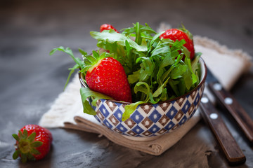 Close up of fresh salad with strawberry and arugula leaves. Ruccola salad in bowl over dark background