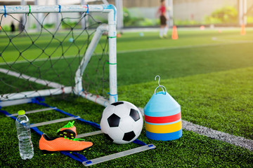 goal, soccer ball, marker cones, sports shoes and bottle water on green artificial turf