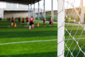 White goalposts and mesh of goal with blurry football players