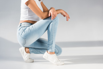 Cropped view of stylish woman in jeans sitting on grey background