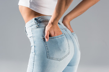 Cropped view of stylish woman in jeans with hands in pockets isolated on grey