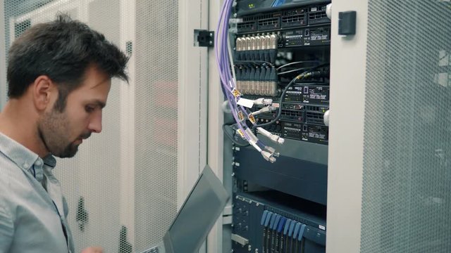 Server IT Engineer In Data Center Server Room.Network Engineer Working Laptop Computer.Server Rack Room Works.Programmer Checks A work Of Server At A Data Center. 