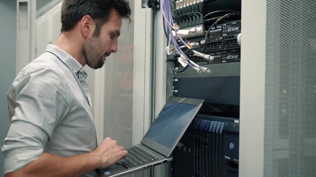 Server IT Engineer In Data Center Server Room.Network Engineer Working Laptop Computer.Server Rack Room Works.Programmer Checks A work Of Server At A Data Center. 