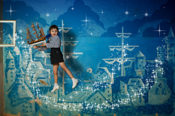 a small beautiful girl flies with a ship on a blue background where houses and ships are painted