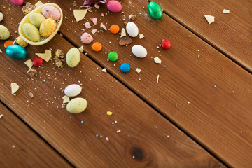 easter, sweets and confectionery concept - chocolate egg and candy drops on wooden table