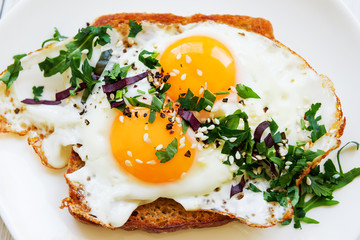 Fried egg with two yolks on bread with chopped greens on a white dish view from the top
