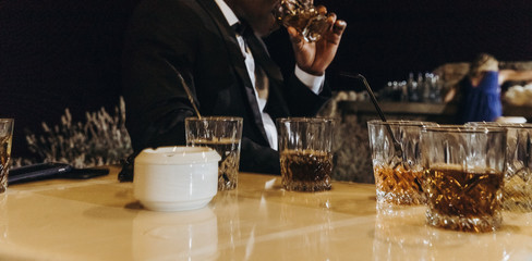 Glasses with whisky stand on the table before man in classy black suit
