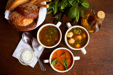 soups menu. 3 types of soups on a wooden table with a bread basket, spices, olive oil, a spoon and a white sauce