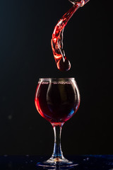 A small glass with wine on a black background and splashes nearby