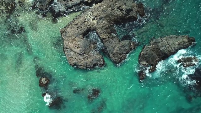 Aerial top view of sea waves crushing into the rocks near beach. Drone shot of sea waves on the dangerous stones.