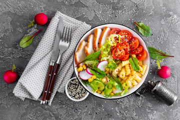 Grilled chicken meat with fresh vegetable salad of tomato, cucumber, radish, lettuce, mangold leaves, corn and pasta for lunch, top view
